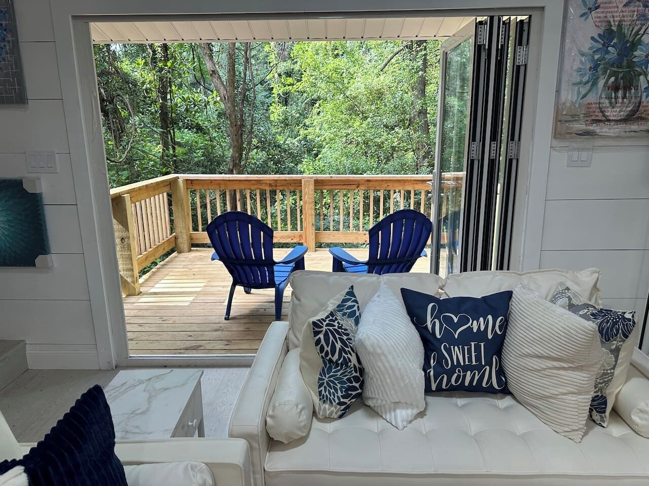 Una habitación con un sofá blanco, sillas azules y una terraza de madera con barandilla.