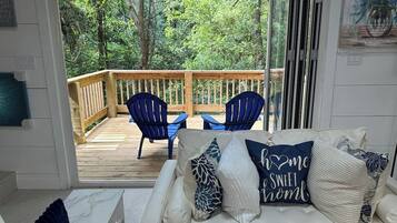 Una habitación con un sofá blanco, sillas azules y una terraza de madera con barandilla.