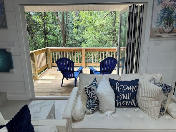 A room with a white sofa, blue chairs, and a wooden deck with a railing.