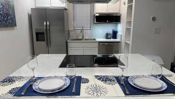 Una cocina moderna con una isla central, electrodomésticos de acero inoxidable y una zona de comedor preparada para dos.
