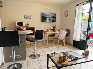 A modern kitchen with a dining area, a bar stool, a TV, and a clock on the wall.