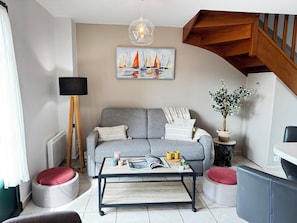 A living room with a sofa, coffee table, and a painting of sailboats.