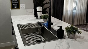 Una cocina con encimera de mármol blanco, un lavamanos integrado, un perchero, una planta en maceta y un cartel que dice "WELCOME TO 4TH AVE ENJOY YOUR STAY".