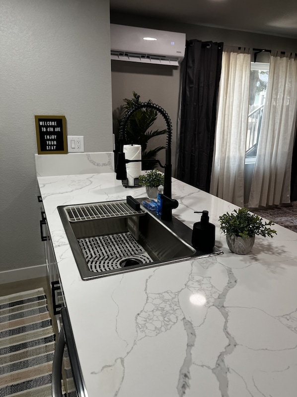 A kitchen with a white marble countertop, a built-in sink, a towel rack, a potted plant, and a sign that reads "WELCOME TO 4TH AVE ENJOY YOUR STAY".