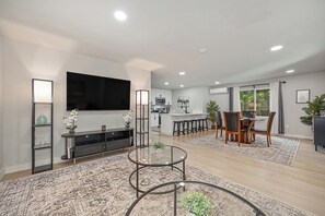 Una sala de estar moderna con un televisor de pantalla plana, una mesa de centro de vidrio y una zona de comedor con una mesa y sillas de madera.