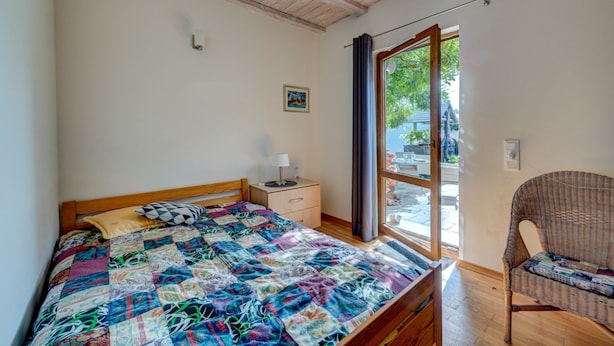 Un dormitorio con cama de madera, una mesita de noche, una silla de mimbre y una ventana con cortinas.