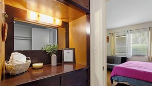 Un dormitorio con un aparador de madera, un cuadro enmarcado, una planta en maceta y una cama con una manta rosa.