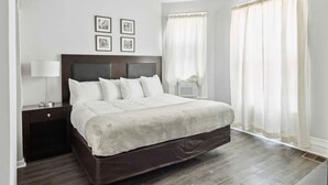 A neatly arranged bedroom with a large bed, a bedside table with a lamp, and a wall-mounted air conditioner. - Detroit 3BR Retreat w/ Wi-Fi + Street Parking (Detroit)