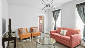 A modern living room with a television, two orange armchairs, a red sofa, a glass coffee table, and a contemporary ceiling light. - Detroit 3BR Retreat w/ Wi-Fi + Street Parking (Detroit)