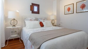 A neatly arranged bedroom with a bed, two bedside tables, a lamp, and framed artwork on the wall. - San Bernardo ático de 1 dormitorio (Sevilla)