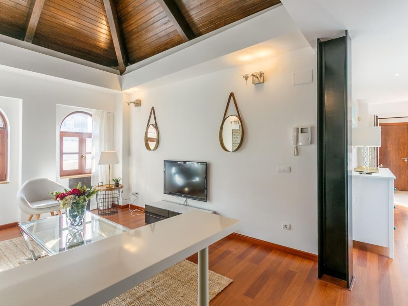 A modern living room with a TV, wooden flooring, and a dining area with a glass table.