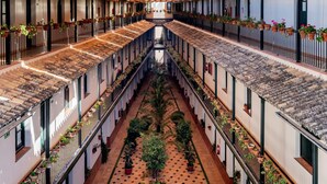 Ein Innenhof mit einem zentralen Weg, gesäumt von Gebäuden mit Terrakotta-Dächern und Streifenmarkisen.