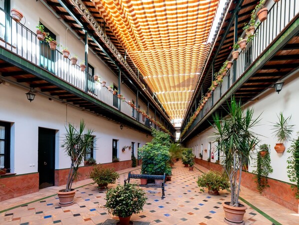 A courtyard with a checkered floor, potted plants, a bench, and a striped ceiling.