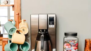 A coffee station with a coffee maker, mugs, and a jar of snacks. - Boyne Mtn Views! 2BR w/ Patio & Fire Pit Access (Boyne Falls)