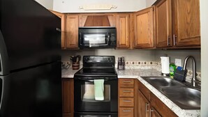 A kitchen with wooden cabinets, a black refrigerator, a microwave, an oven, and a sink. - Boyne Mtn Views! 2BR w/ Patio & Fire Pit Access (Boyne Falls)