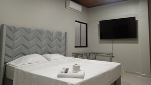 A hotel room with a bed, a ceiling fan, an air conditioning unit, a TV mounted on the wall, and a window. - Alojamiento Casa Luna (Iquitos)