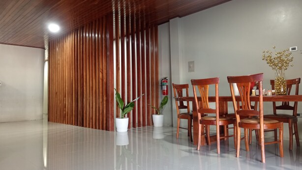 A modern interior with a polished floor, wooden panel wall, and a dining area with wooden chairs and a vase of flowers. - Alojamiento Casa Luna (Iquitos)