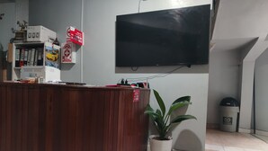 A reception desk with a flat-screen TV mounted on the wall, a potted plant, and a trash bin. - Alojamiento Casa Luna (Iquitos)