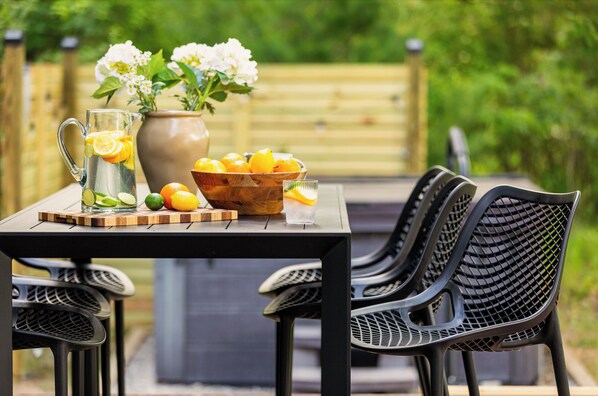 Un espace de restauration en plein air avec une table dressée pour deux personnes, une carafe de limonade, un bol de citrons et un vase rempli de fleurs.