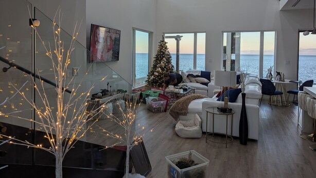 A spacious living room with a large Christmas tree, a glass tree sculpture, and a view of the sea.