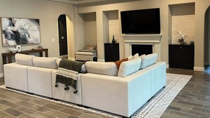 A modern living room with a sectional sofa, a flat-screen TV, a fireplace, and a ceiling fan.