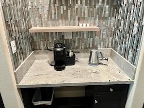 Uma cozinha compacta com cafeteira, chaleira e prateleira sobre o balcão.
