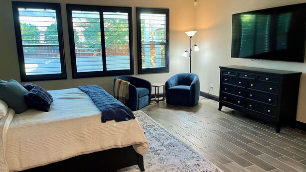 A bedroom with a bed, two chairs, a dresser, and a TV.