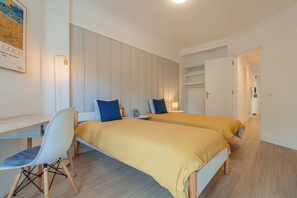 A modern hotel room with two beds, a desk, and a chair.