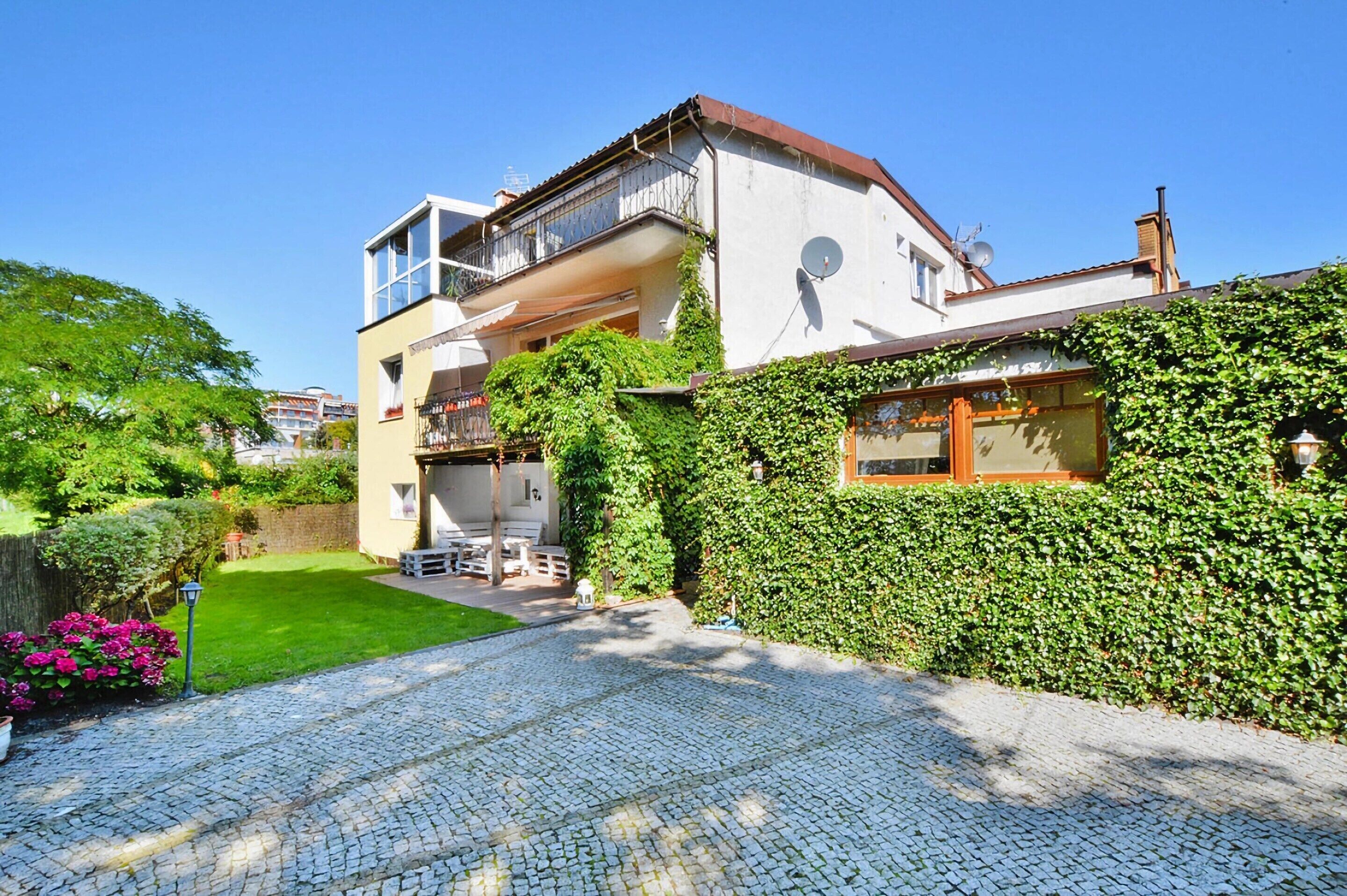 A two-story house with a balcony, a satellite dish, and a well-maintained garden.