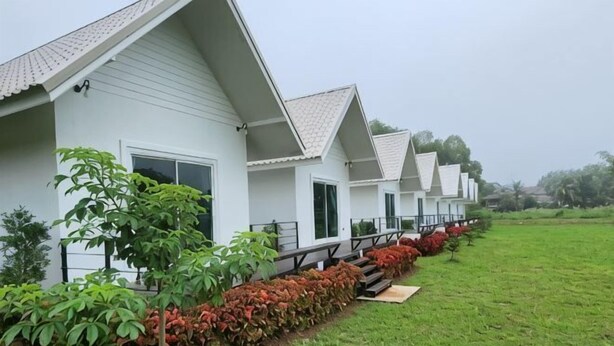 A row of white buildings with flat roofs, each with a balcony and a small garden area. - Casa Camp (Khao Kho)