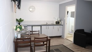 A compact kitchen with white cabinets, a microwave, and a dining area with a wooden table and chairs. - Spanish Lace Motor Inn (Rosslea)