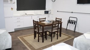 A compact kitchen with a microwave, a sink, and a blackboard. There is a dining table with chairs and a small rug. A TV is mounted on the wall, and a towel rack is visible. - Spanish Lace Motor Inn (Rosslea)