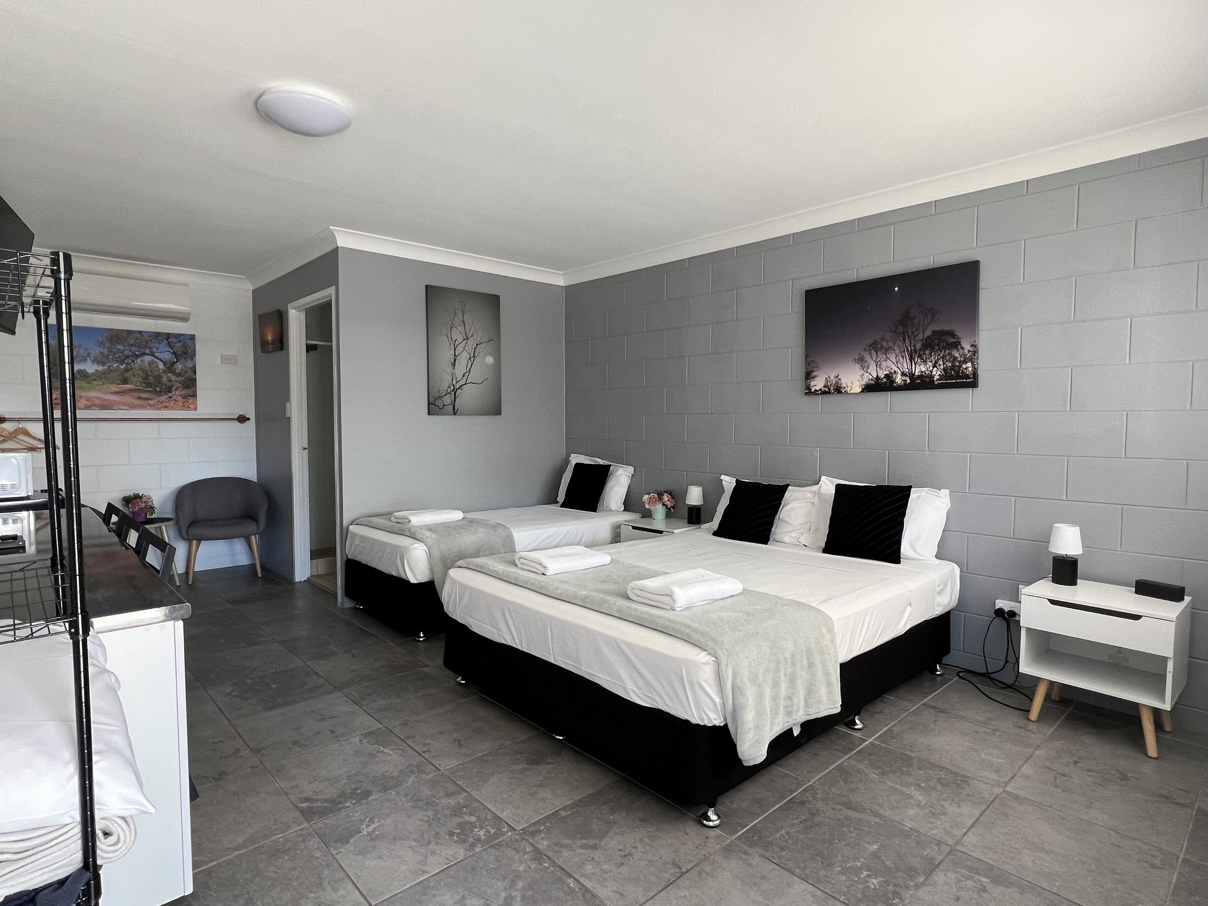 A modern hotel room with two beds, grey tiled flooring, and a grey brick wall.
