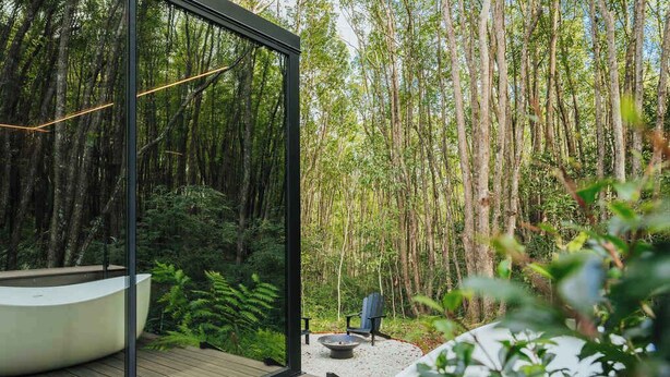 Una habitación moderna con paredes de vidrio, una terraza de madera, un jacuzzi y una chimenea.