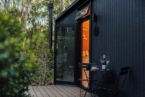 Une terrasse en bois avec une table et des chaises, une bouteille de vin et un verre.