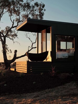 A modern cabin with a large window, a boat-shaped seating area, and a tree in the foreground. - Heathcote Winery Stay with Sweeping Hilltop Views (Toolleen)