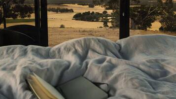 A bed with a book, large windows, and a view of trees and water.
