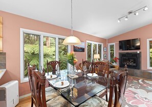 A dining room with a glass table, wooden chairs, a chandelier, and a fireplace.