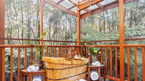 Ein hölzernes Whirlpool-Becken mit Handtüchern und einem kleinen Tisch, umgeben von einer Holzterrasse mit Geländern und einer Glaskuppel.