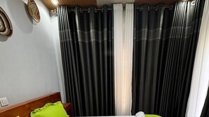 Una habitación de hotel con una cama grande, ropa de cama verde y blanca, un cabecero de madera y cortinas blanco y negro.