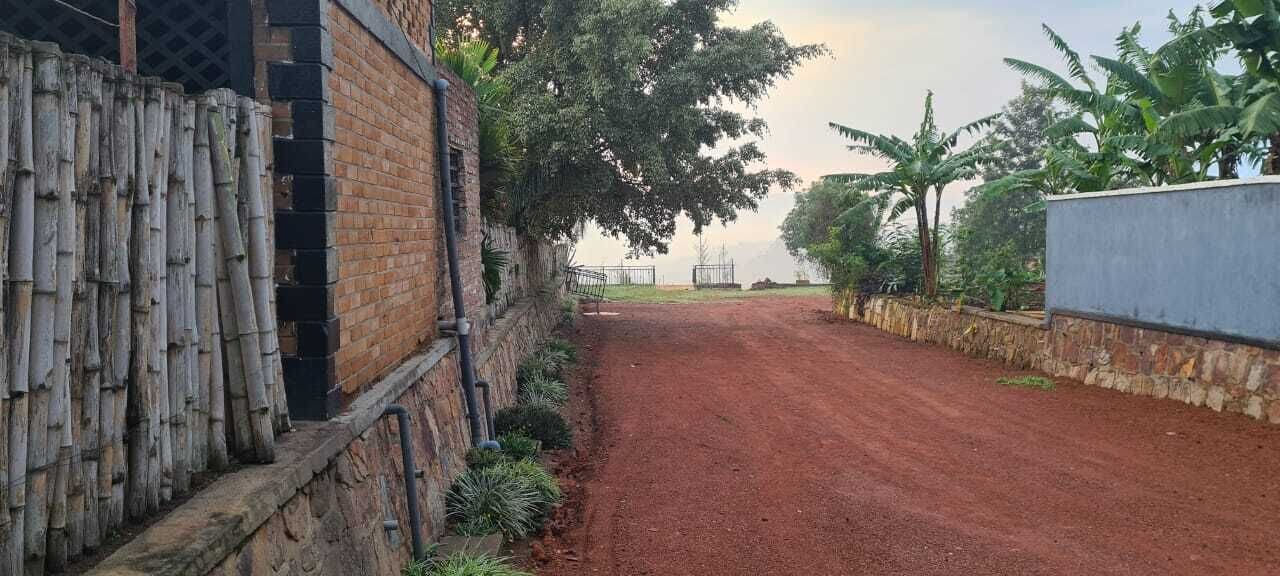 Un chemin de terre bordé d’une clôture en bambou et d’un mur de briques.