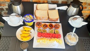 Una mesa servida con pan, fruta, una taza de café y dos cafeteras.