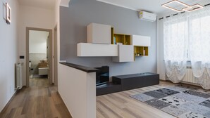 Ein modernes Wohnzimmer mit integriertem Fernseher, einer grauen Wand mit Regalen, Holzboden und einem gemusterten Teppich.