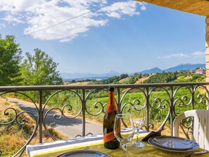 Ein Tisch draußen gedeckt, mit einer Flasche und Gläsern, mit Blick auf eine malerische Landschaft mit Bergen und Grün.