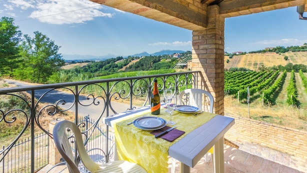 A balcony with a table set for two, overlooking a vineyard.