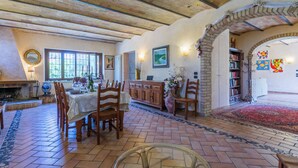 A dining area with a brick floor, wooden chairs, a table set for a meal, a fireplace, and a bookshelf with books and decorative items.