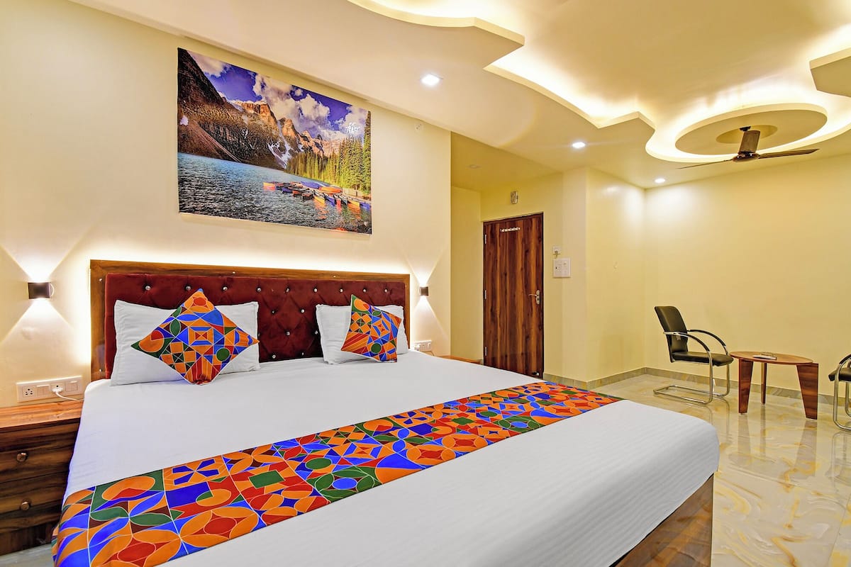 A hotel room with a large bed, a painting of a mountain landscape, a desk with a chair, and a ceiling fan.