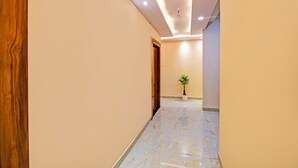 A hallway with a marble floor, wooden door, and a potted plant. - Fabhotel Rj (Patna)