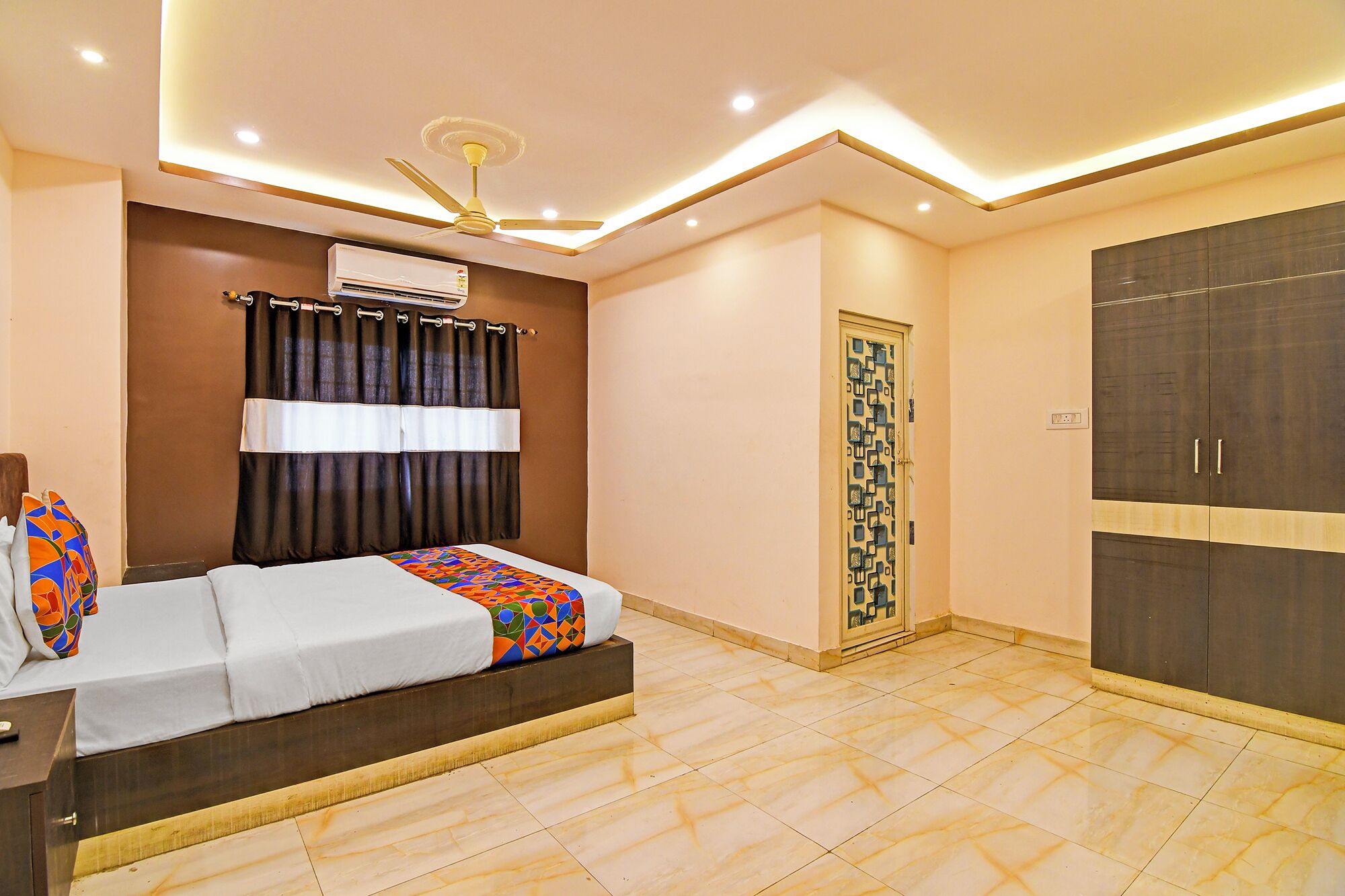 A bedroom with a bed, an air conditioner, a ceiling fan, a wardrobe, and a decorative door.