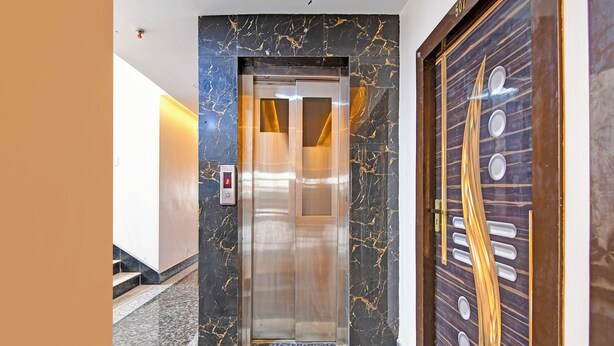 Un ascensor con pantalla digital, paredes de mármol y puerta de madera con pomos redondos.